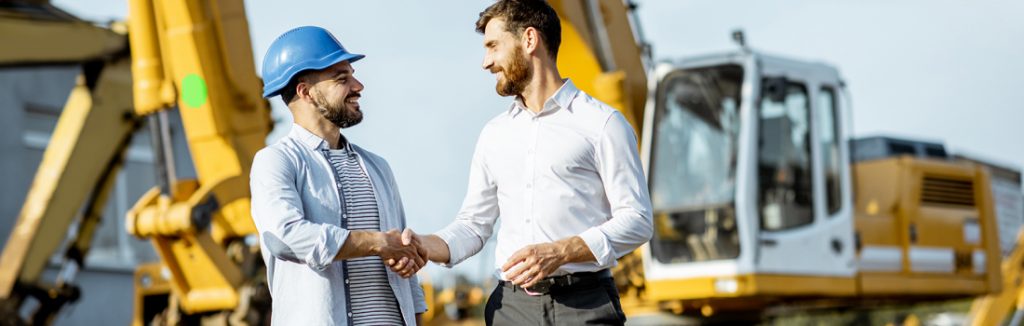 Two men shaking hands while standing in front of construction equipment
