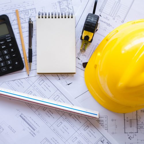 hard hat, calculator, notepad, and rule sitting on top of blueprints